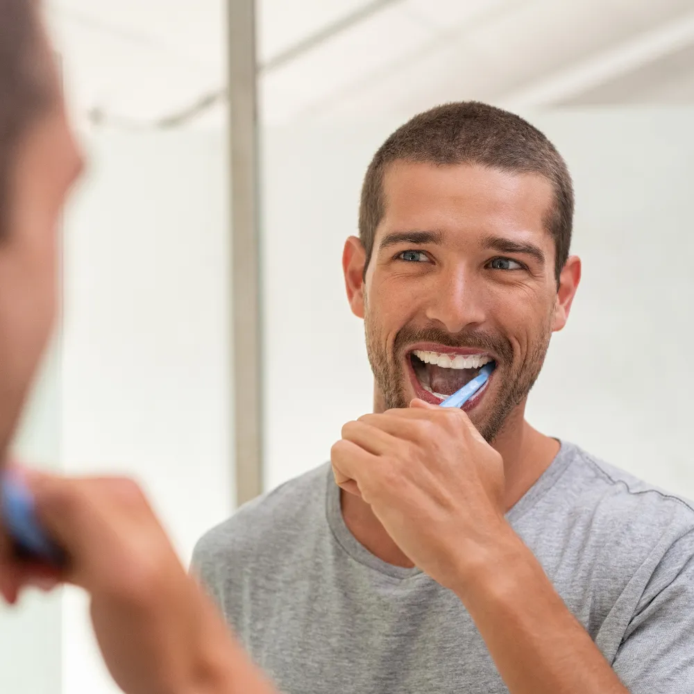 Man brushing teeth to maintain dental veneers and oral health