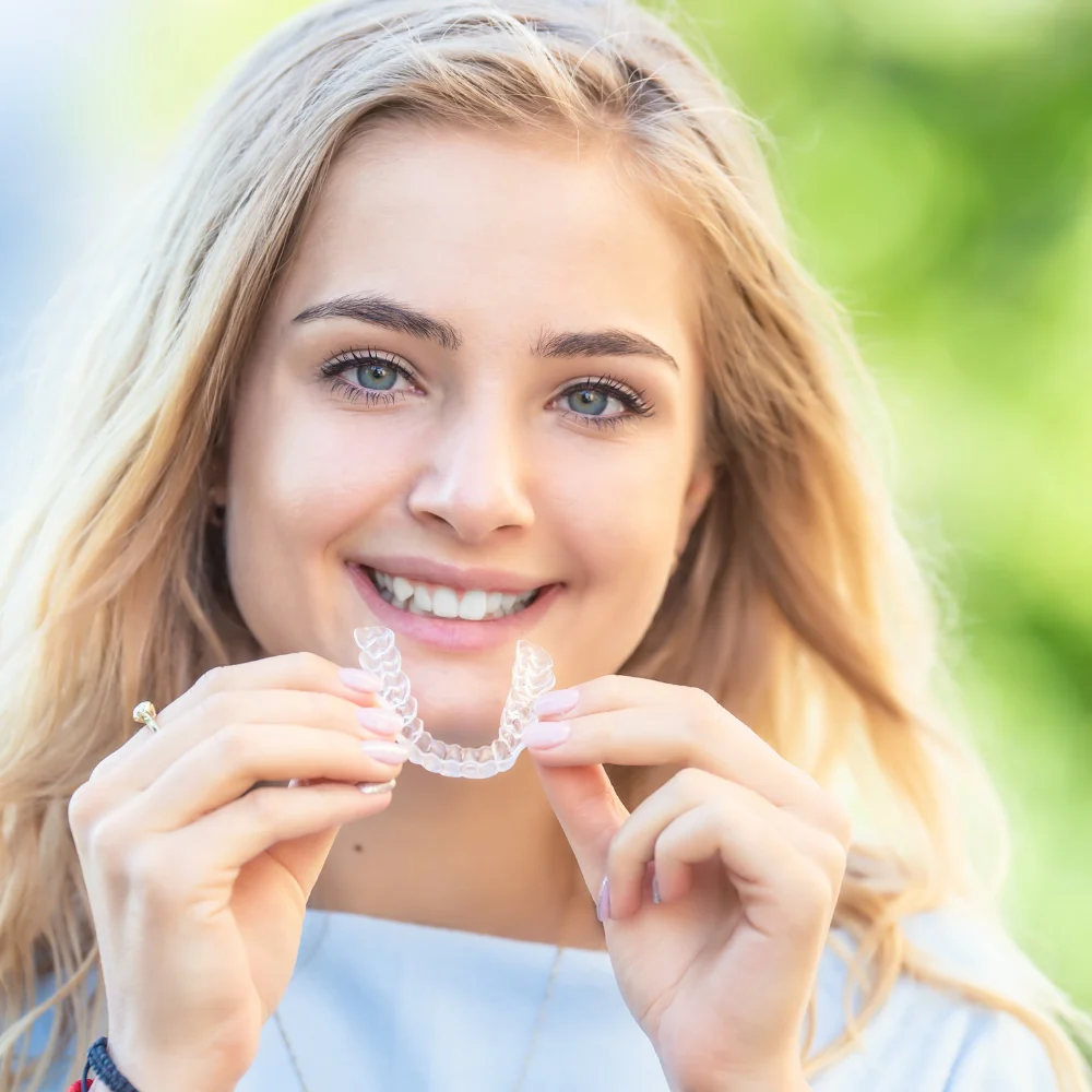 Patient smiling while holding Invisalign aligners before treatment